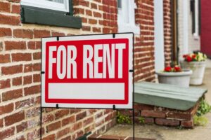 Red "For Rent" sign displayed in front of a brick townhouse.