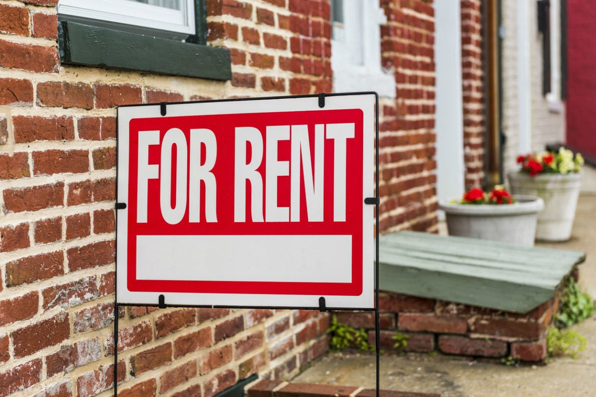 Red "For Rent" sign displayed in front of a brick townhouse.